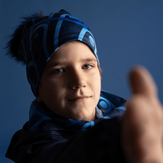 A young boy wearing the Mechanic Blue beanie and giving a thumbs-up, set against a blue background.