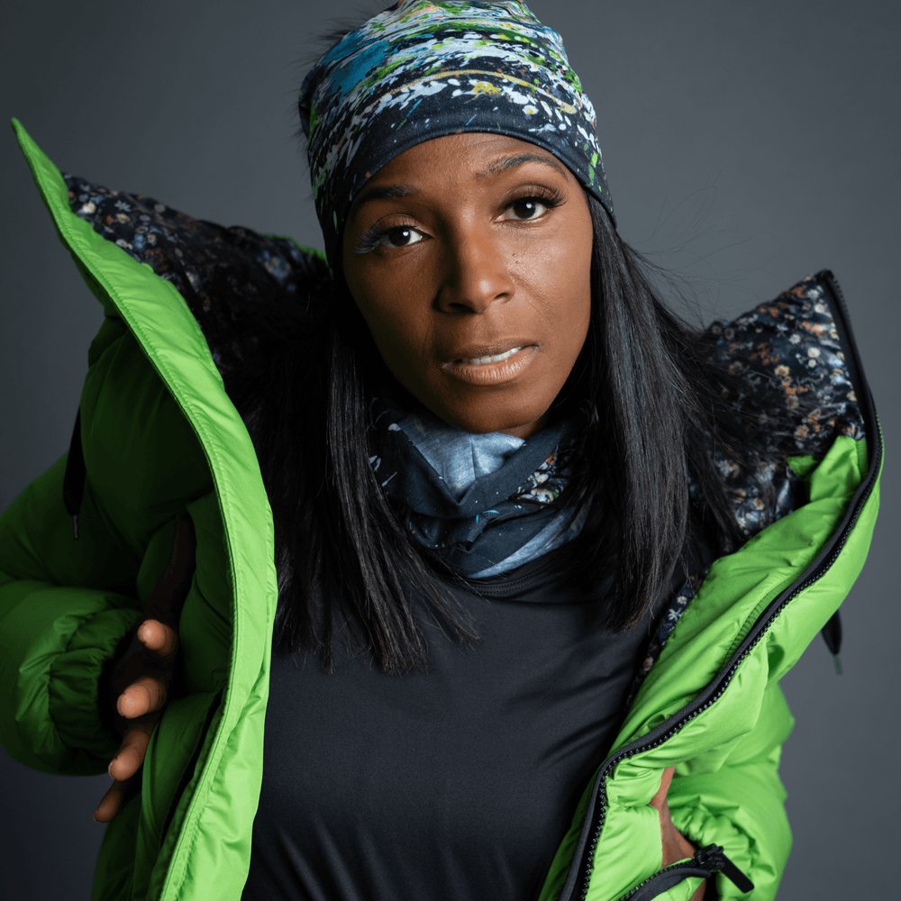 Model wearing a green puffer jacket and a beanie and neck tube with a floral and abstract art print.