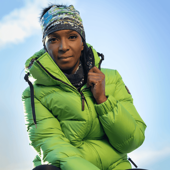 Woman looking up, wearing the Meduse Beanie as a headband and a green puffer jacket.