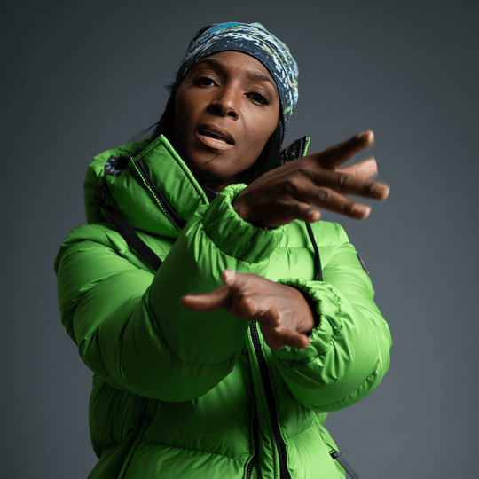 Woman in a green puffer jacket, gesturing, wearing the Meduse Beanie as a headband.