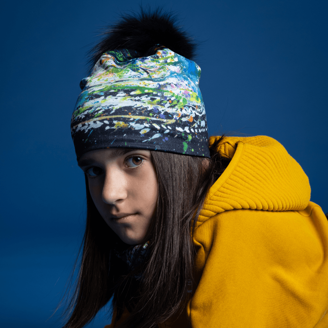 Young girl wearing the Meduse Beanie with abstract art and a black pompom.