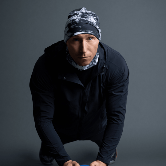 Man in a black jacket wearing a black and white abstract pattern beanie and neck gaiter, in a push-up pose.