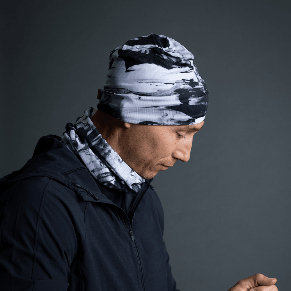Man wearing a black and white abstract pattern beanie and matching neck gaiter, paired with a black jacket.