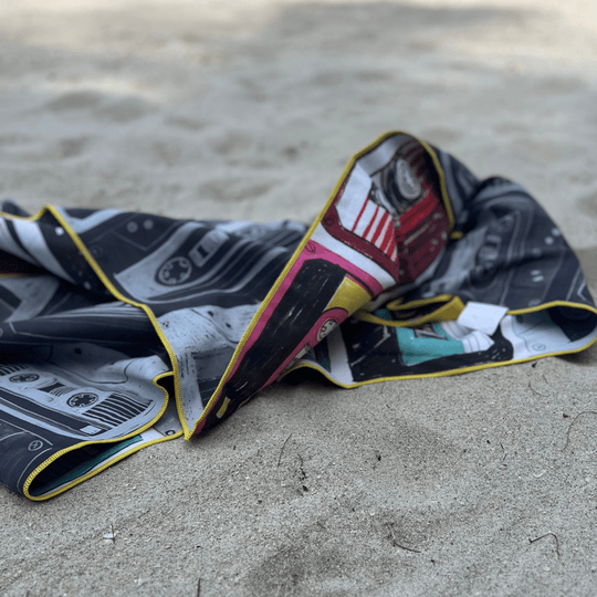 Close-up of the folded Mixtapes beach towel on the sand, showing the black and white side and colorful edge.