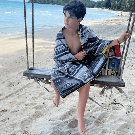 Child sitting on a wooden swing on a beach, wrapped in the black and white side of the Mixtapes beach towel.