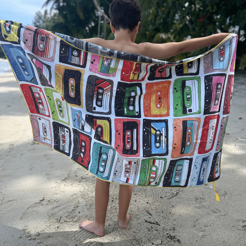 Child on a beach holding up the colorful side of the Mixtapes reversible beach towel.