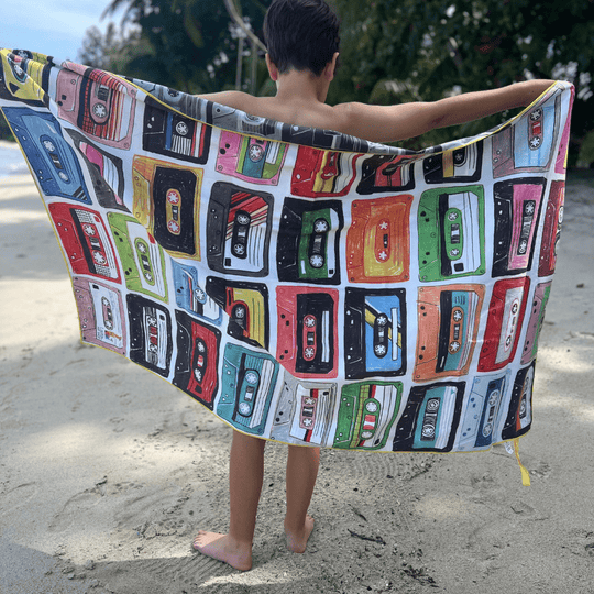 Child on a beach holding up the colorful side of the Mixtapes reversible beach towel.