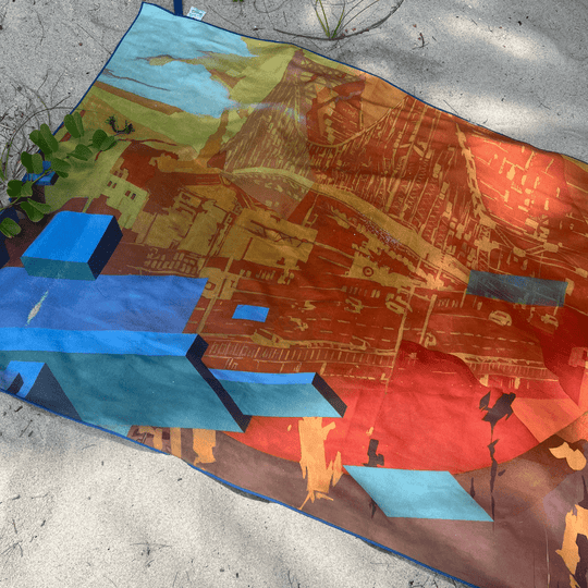 Towel laid out on sand with greenery, showing the graffiti-style art design in full.