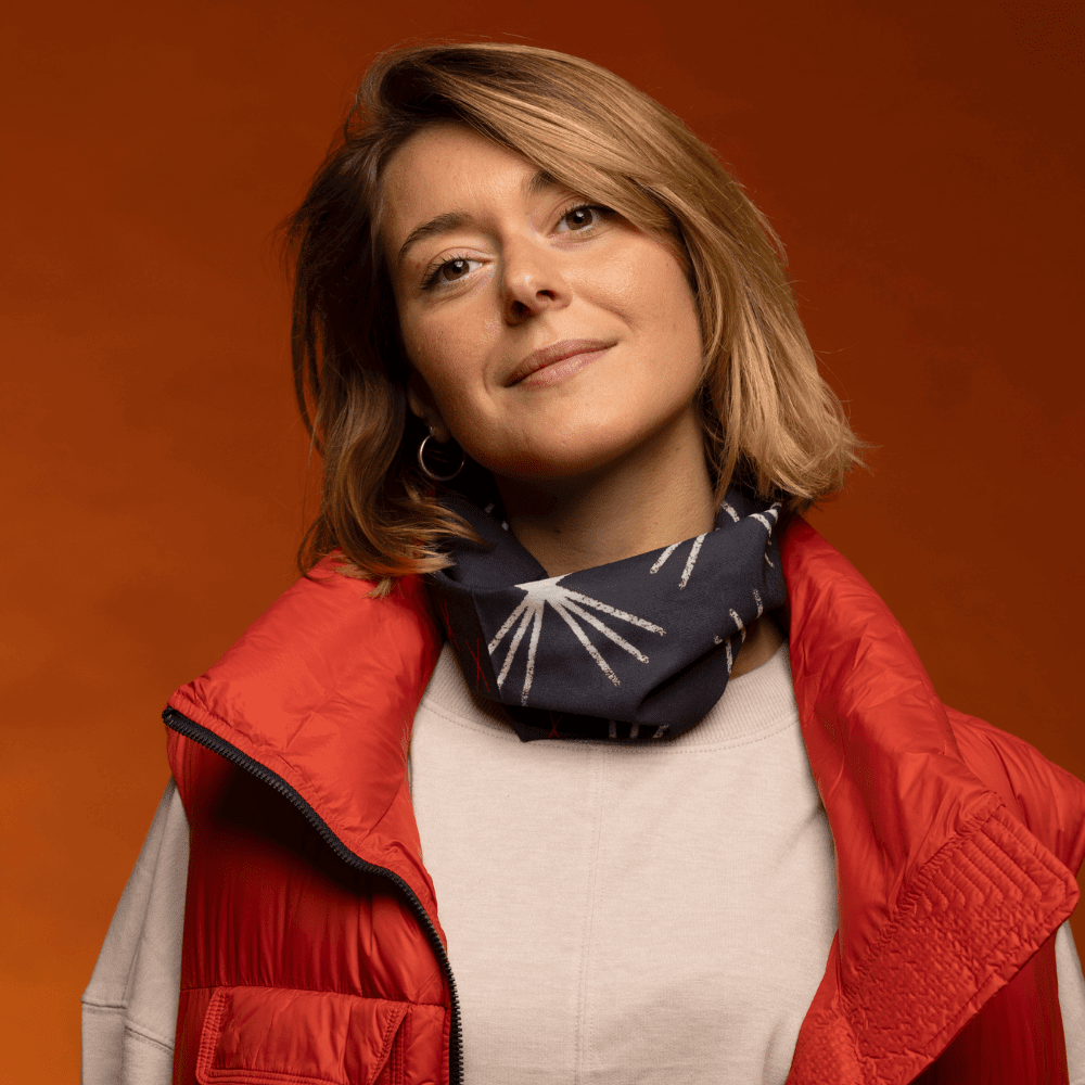 A woman wearing a red vest and a starburst-patterned neck tube casually around her neck.
