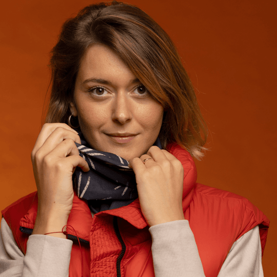 Close-up of a woman adjusting her starburst-patterned neck tube, framing her face with a red vest.