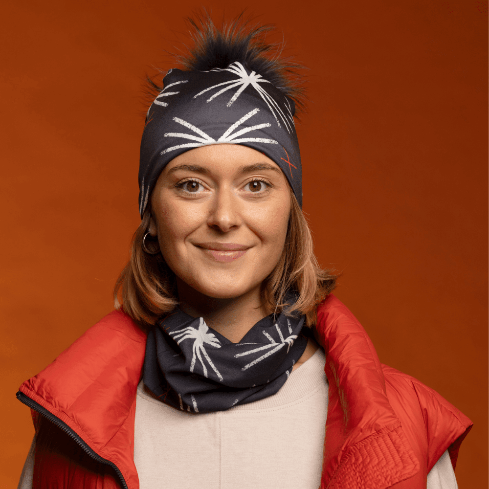 A smiling woman wearing a red puffer vest and a matching beanie and neck tube with a starburst pattern.