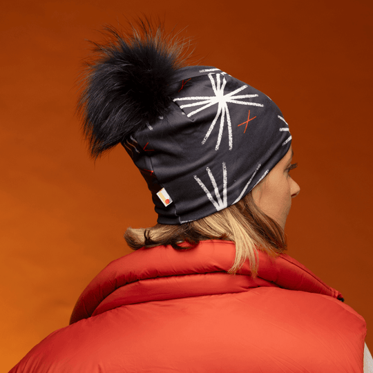 Woman wearing the black MotifX beanie with black pompom, seen from the side and back, with a red puffer vest.