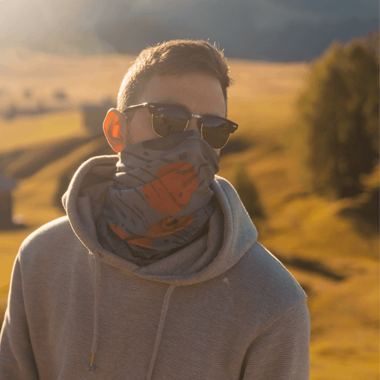 Man wearing a grey hoodie, with the orange, grey, and black multifunction tube pulled up over his nose and mouth.