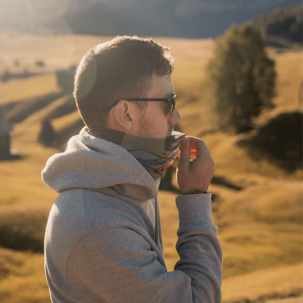 Man wearing a grey hoodie adjusts the orange, grey, and black multifunction tube as a face covering.