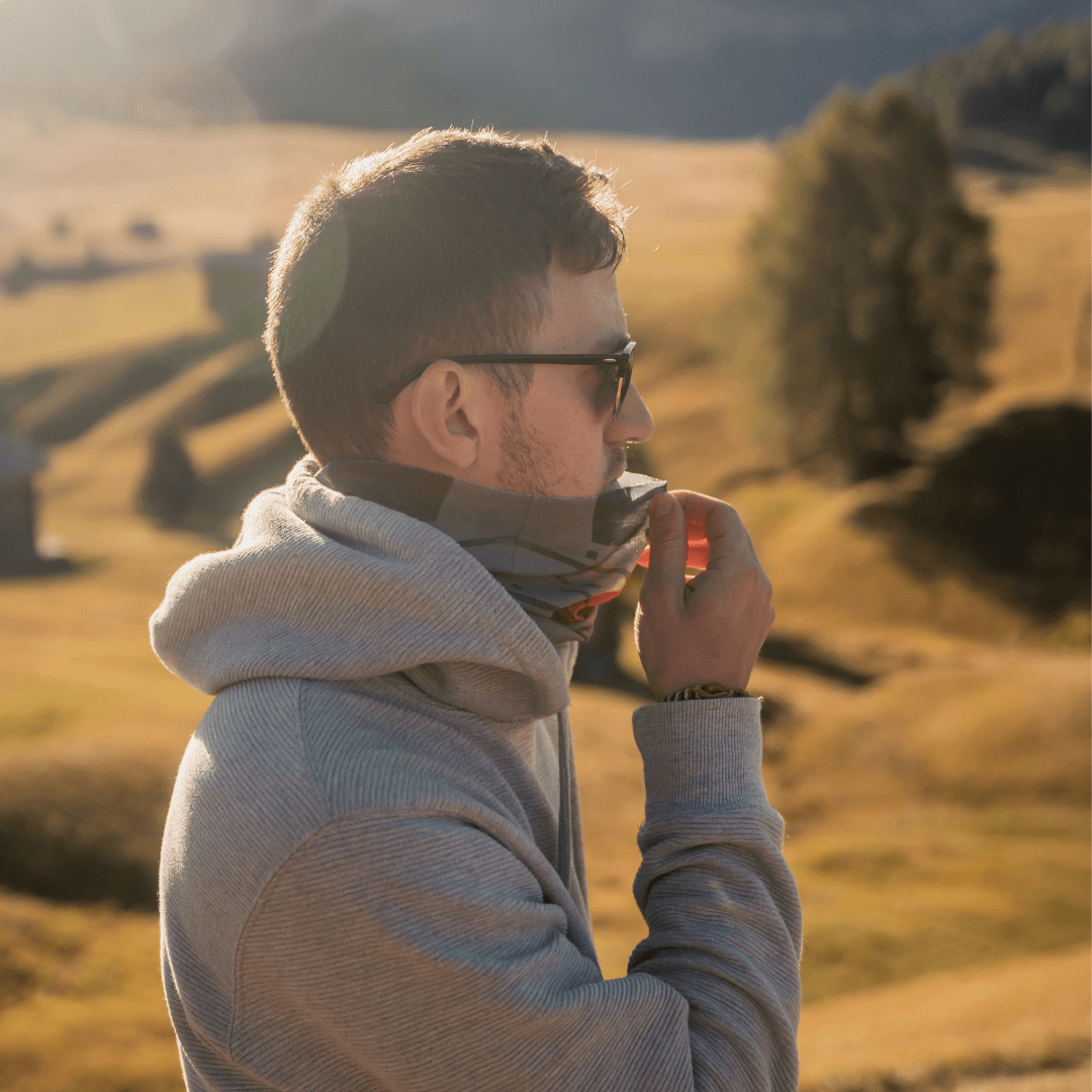 Man wearing a grey hoodie adjusts the orange, grey, and black multifunction tube as a face covering.
