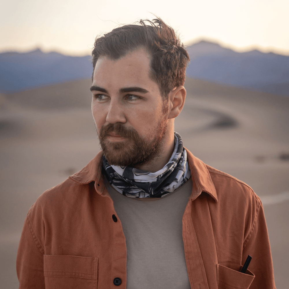 Man with beard wearing the black and white abstract pattern neck gaiter outdoors in a desert landscape.