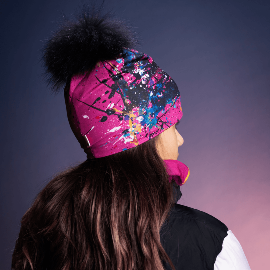 Back view of a teenage girl wearing a pink and black abstract art beanie with a black pompom.