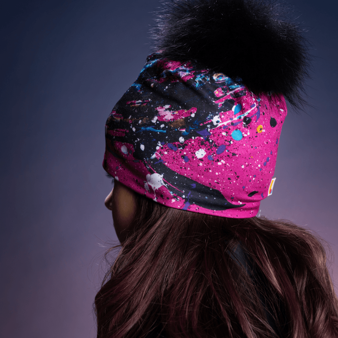 Side profile of a teenage girl wearing a pink and black abstract art beanie with a black pompom.