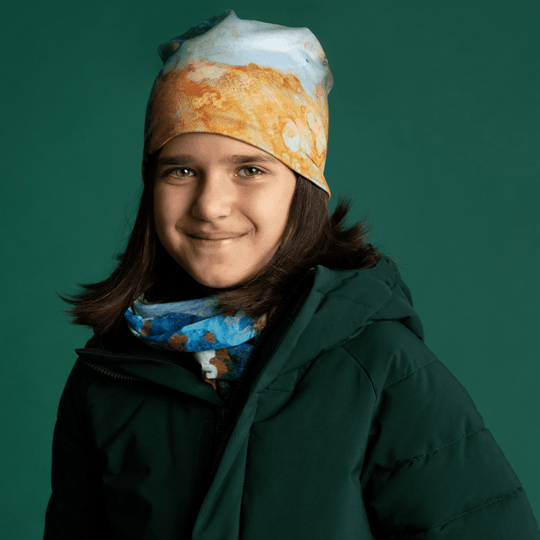 A young girl wearing the Ocean Marble Beanie and matching neck warmer with a dark green winter jacket.