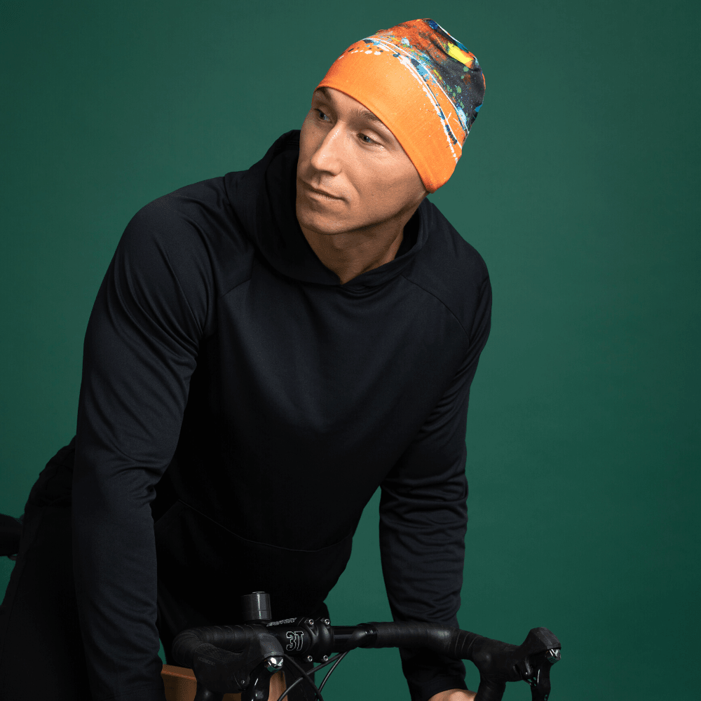Man wearing a black hoodie and the orange abstract art beanie, leaning on a bicycle.