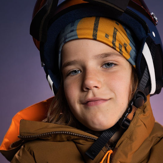 Child wearing a colourful abstract-print beanie under a ski helmet with goggles and a winter jacket, demonstrating helmet compatibility