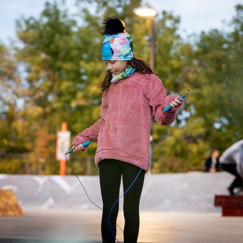 A young girl wearing the Pastel Flowers beanie while jumping rope outdoors at a skate park.