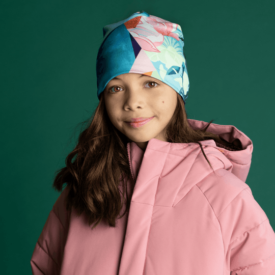 Front view of a young girl smiling, wearing the Pastel Flowers Beanie and a pink winter jacket.