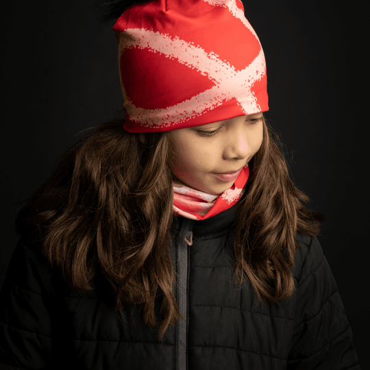 Close-up of a young girl wearing the Peachy-Red Beanie and neck tube against a black background.