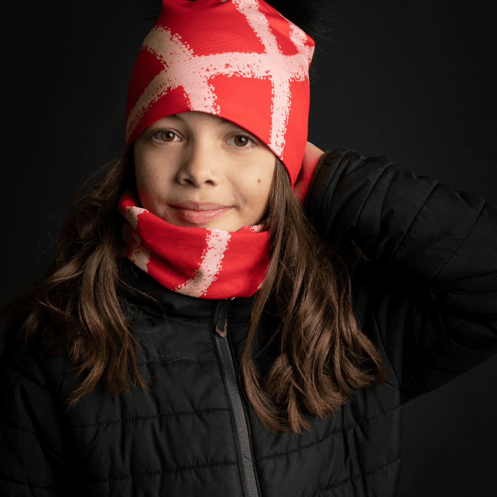 Close-up portrait of a young girl wearing the Peachy-Red Beanie and neck tube, smiling softly.