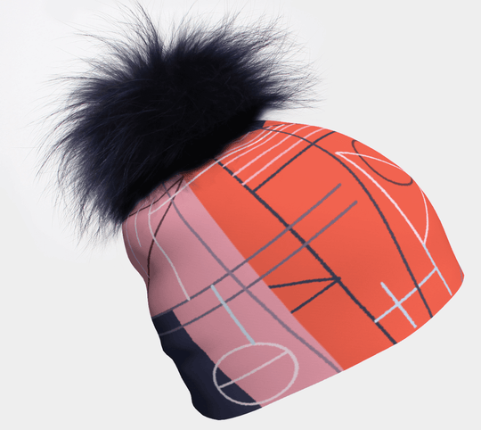Close-up of a pink, blue, and orange abstract graphic print beanie with a large navy blue detachable pompom.
