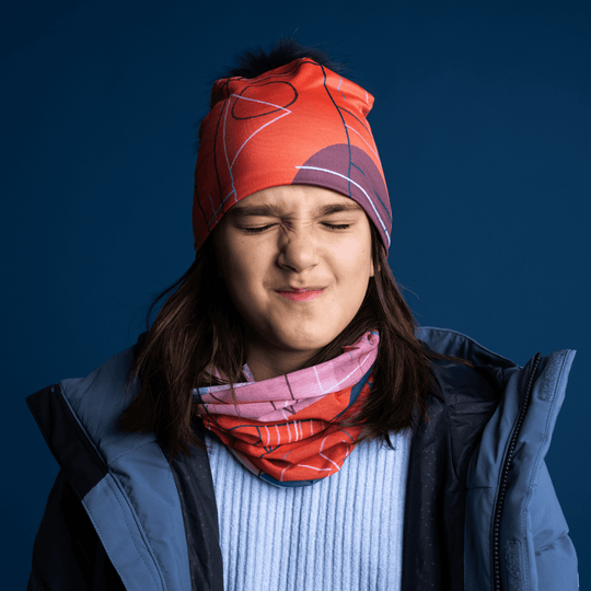 A young girl wearing the Pink Graphicometrics Beanie and neck gaiter, grimacing playfully.
