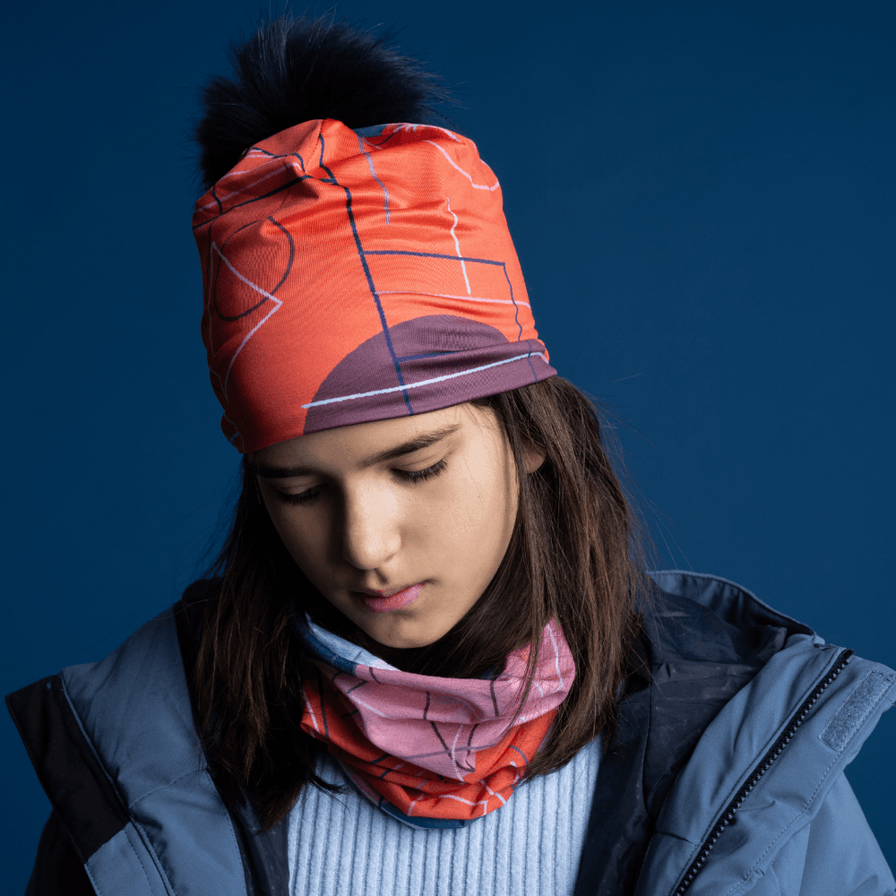 A young girl wearing the Pink Graphicometrics Beanie and a matching neck gaiter, looking down.