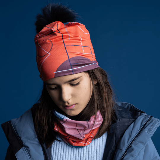 A young girl wearing the Pink Graphicometrics Beanie and a matching neck gaiter, looking down.