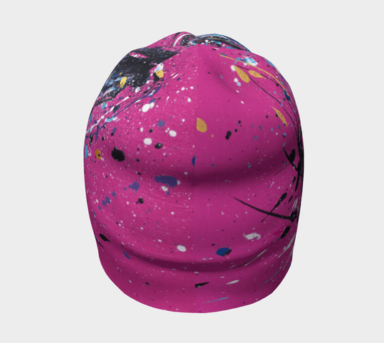 A pink beanie with an abstract paint splatter design, viewed from the front.