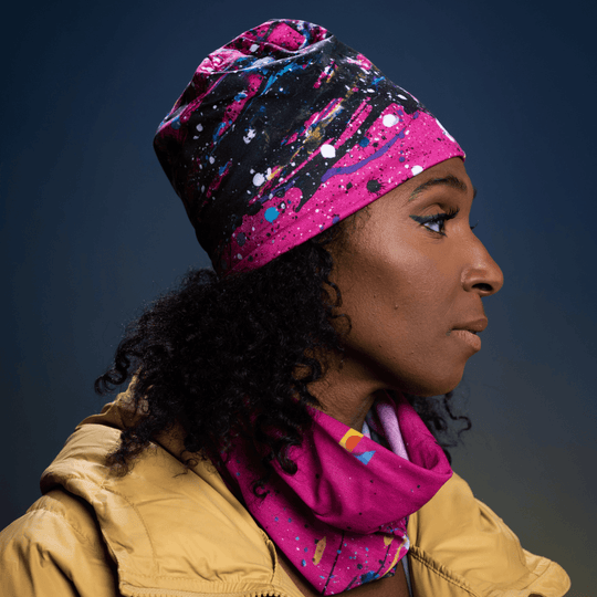 Woman wearing a pink abstract print beanie and matching neck tube in a yellow jacket, side profile.