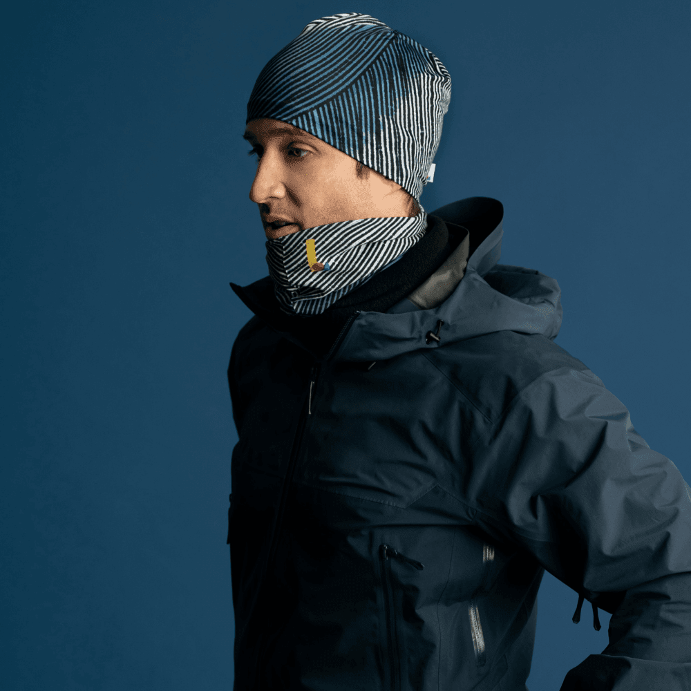 Man wearing a dark ski jacket and a matching abstract lines beanie and neck tube, looking to the side.