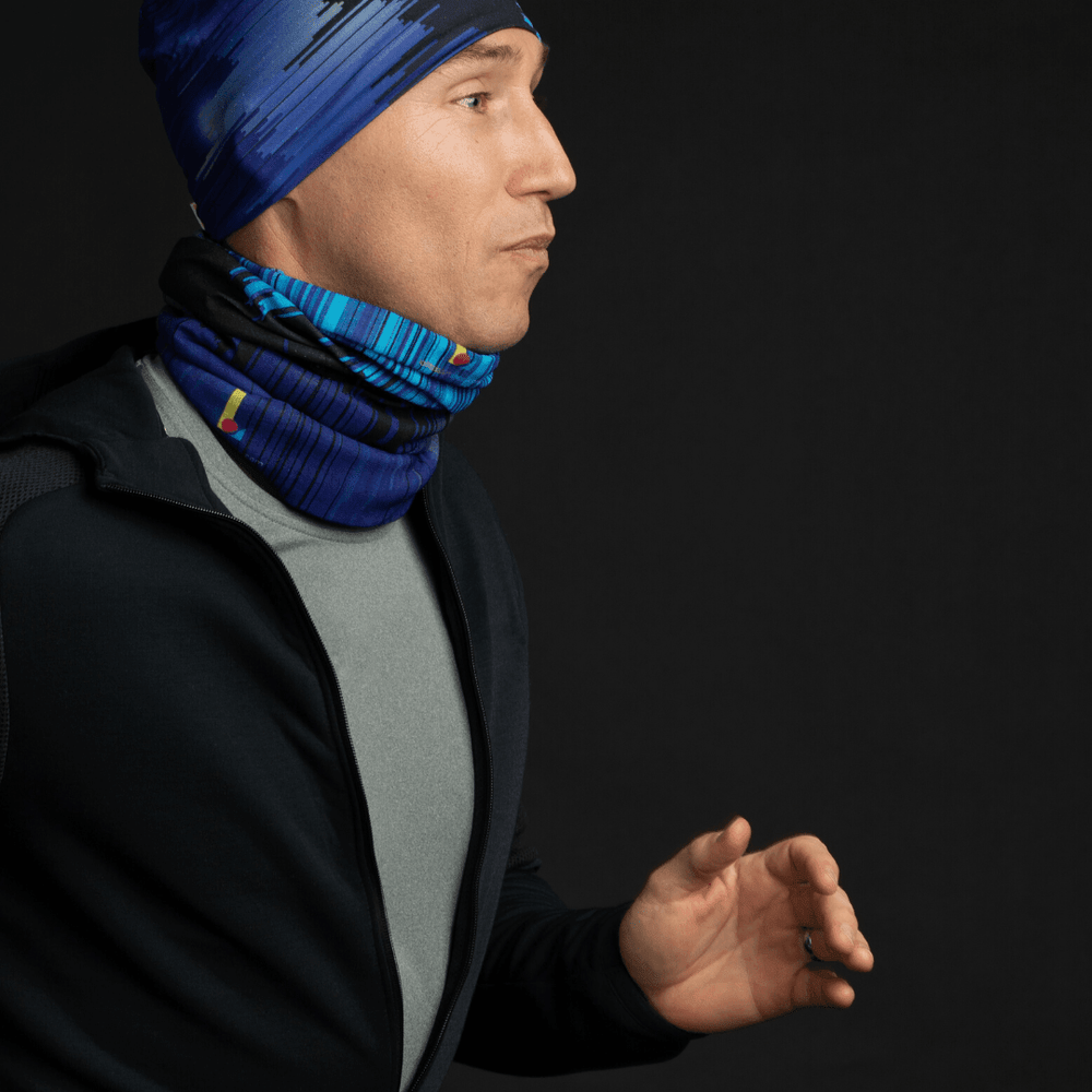 Man wearing a grey t-shirt and dark hoodie, with a blue abstract art beanie and a matching neck gaiter.