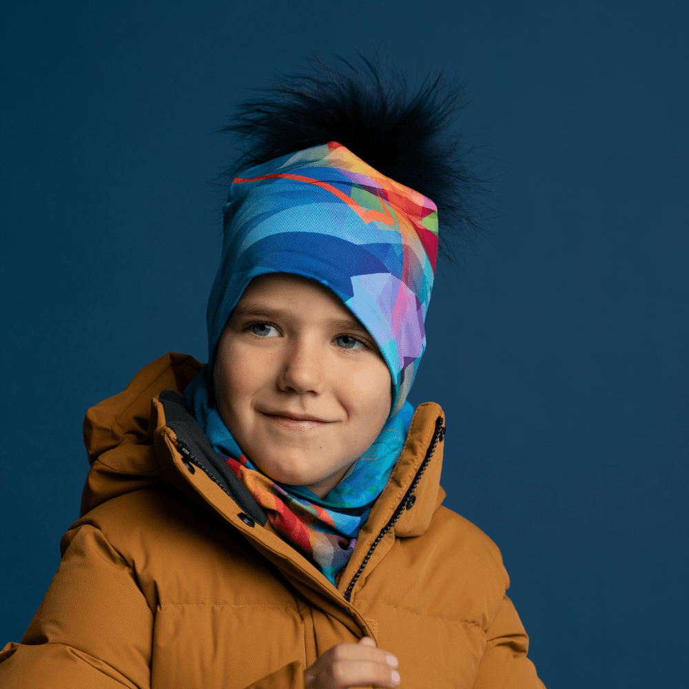 A young boy wearing a mustard yellow winter coat, a matching beanie with a black pompom, and a colorful neck gaiter.