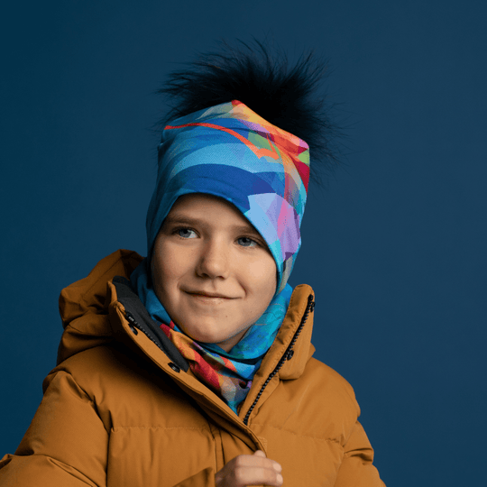 A young boy wearing a mustard yellow winter coat, a matching beanie with a black pompom, and a colorful neck gaiter.