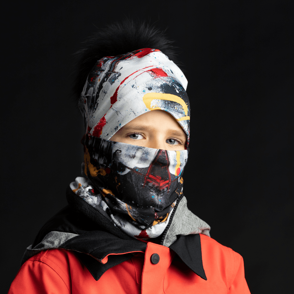A child wearing the red and black abstract art neck tube as a face mask and beanie, part of a ski outfit.