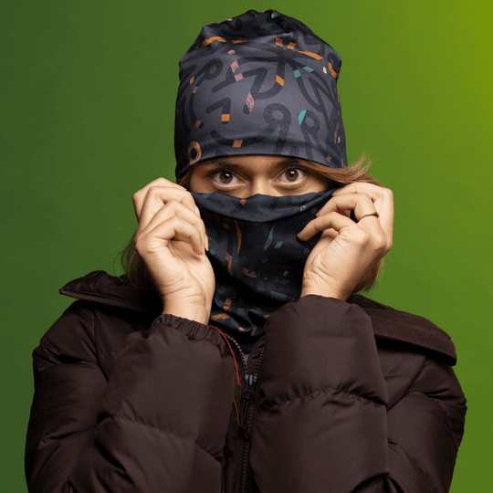 A woman wearing a winter jacket pulls a grey patterned neck tube up over her face, revealing her eyes.