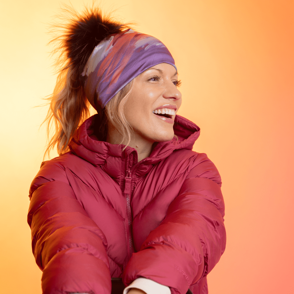 Femme portant la tuque Ponytail Tulips avec pompon noir et une veste rouge, riant.