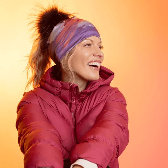 Femme portant la tuque Ponytail Tulips avec pompon noir et une veste rouge, riant.