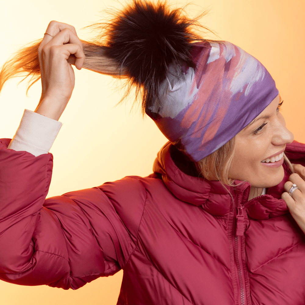 Woman wearing the Ponytail Tulips Beanie with a black pompom, a red puffer jacket, and a ponytail.
