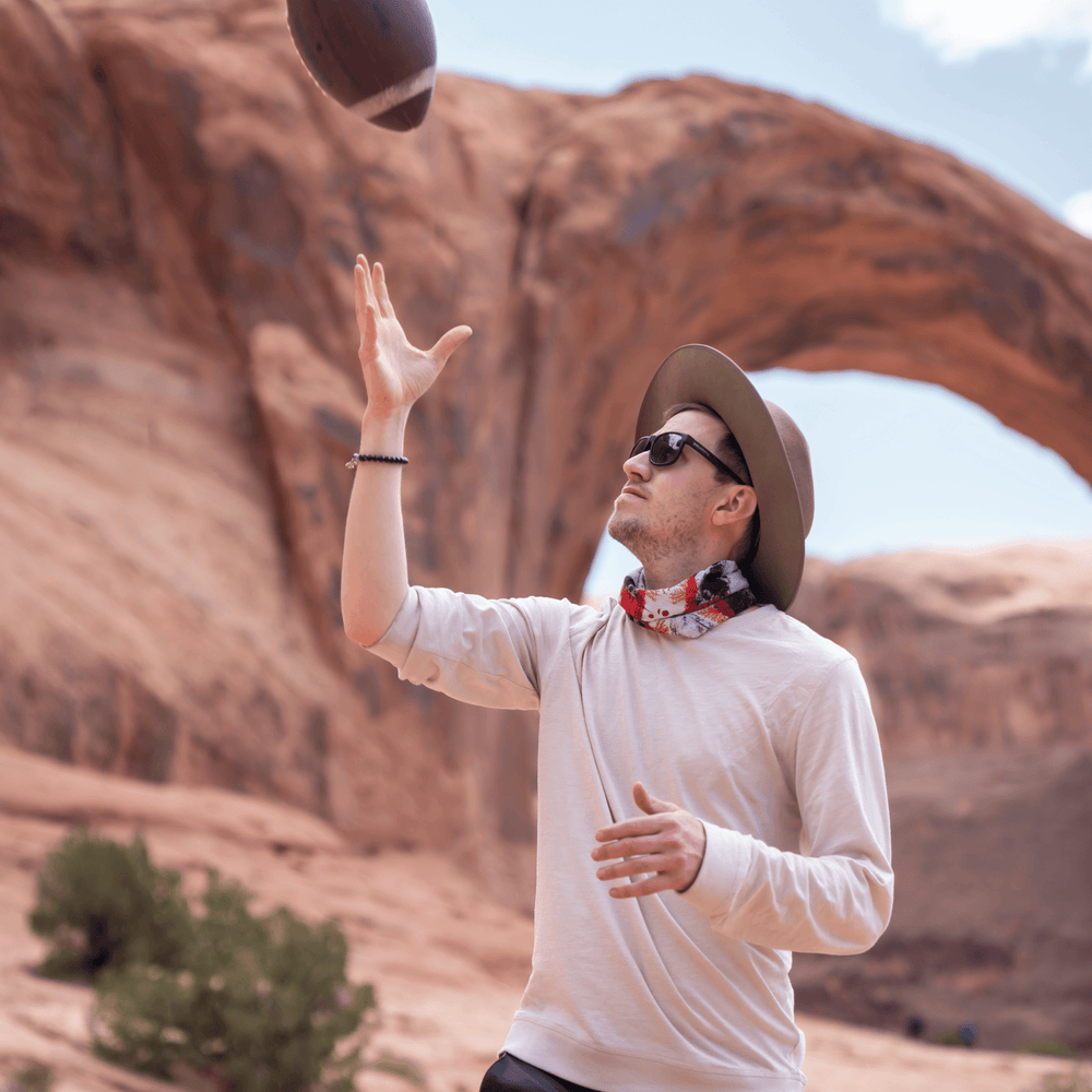 Man wearing a red and white bandana around his neck while throwing a football outdoors.