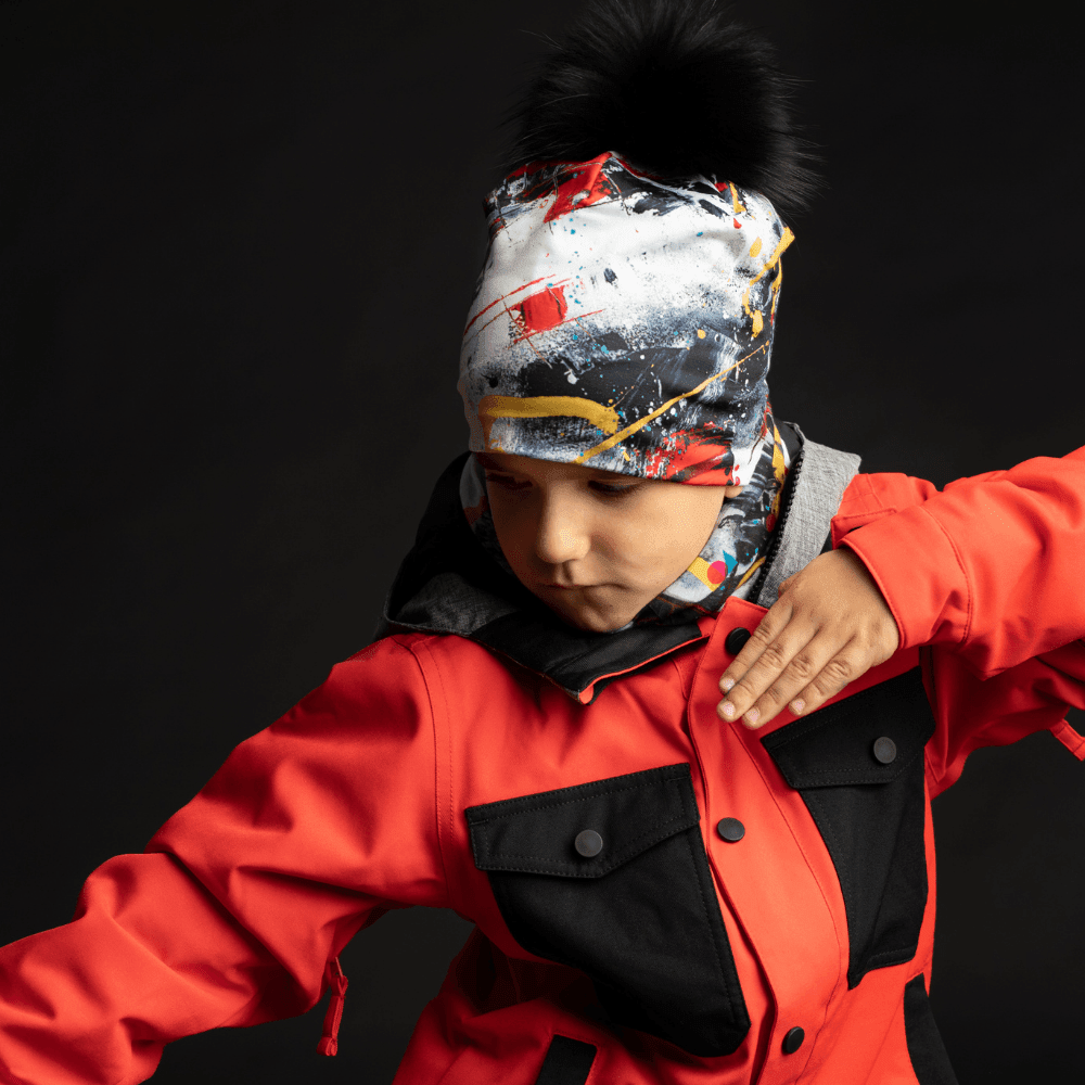 Child wearing the Red and Black Removable Pompom Beanie and a matching neck gaiter, layered under a red ski jacket.