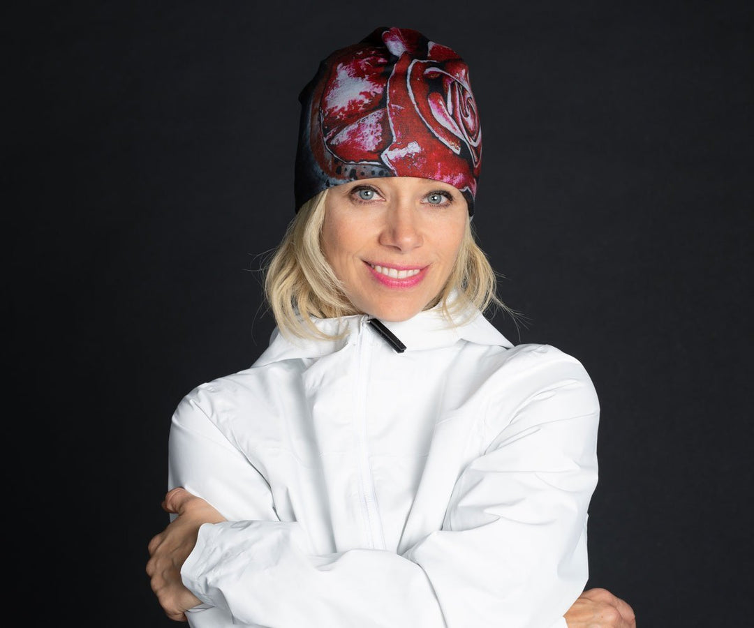 A smiling woman wearing the Red Rose Beanie and a white jacket against a black backdrop.