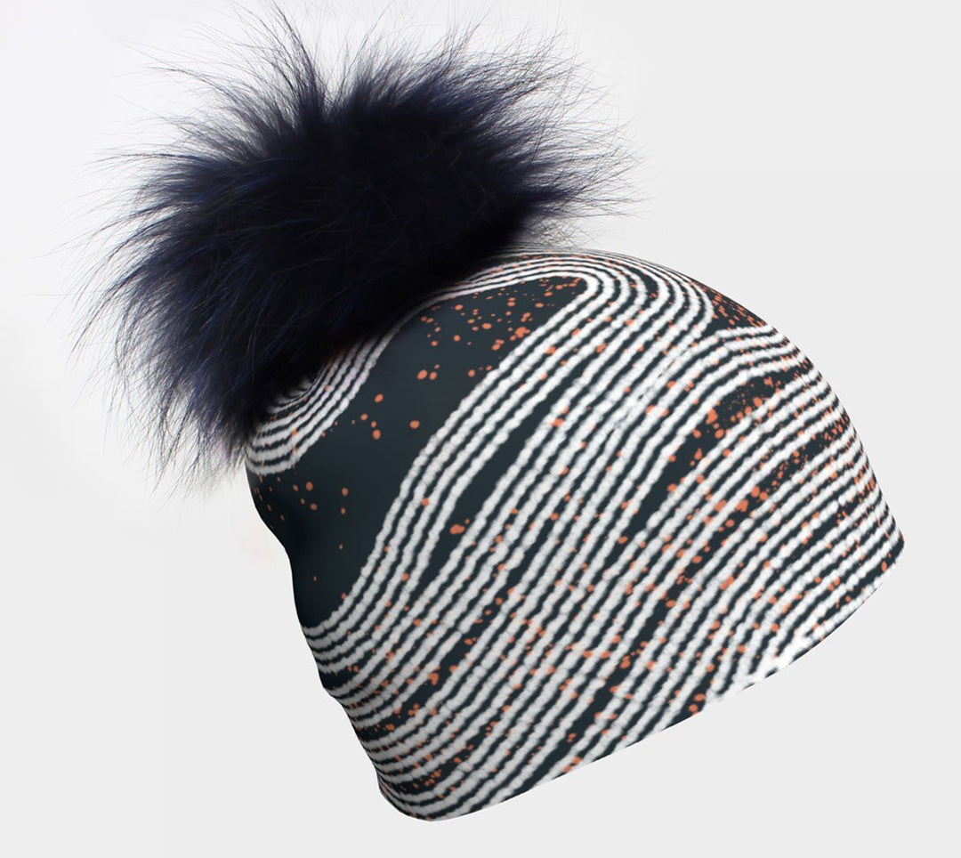 Dark Steel Beanie with a large, fluffy navy pompom and a swirling white and orange abstract stripe pattern.