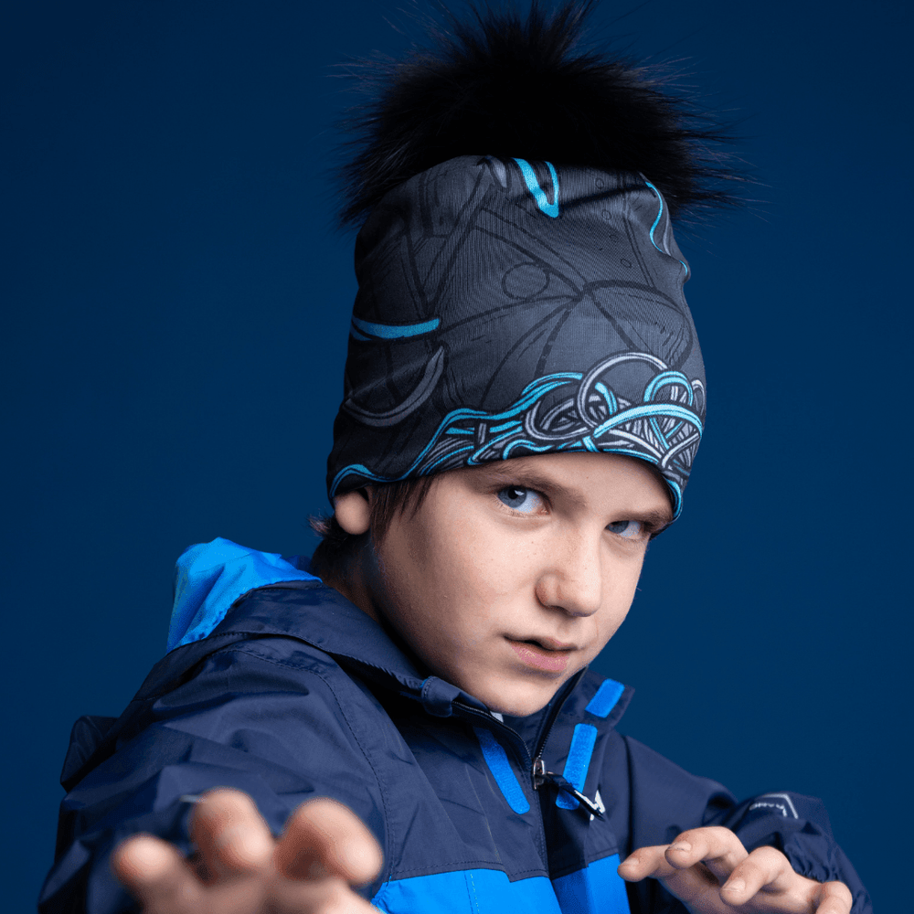 Close-up of a boy wearing the black and blue patterned Robocats Beanie under a blue hooded jacket, looking directly at the camera.