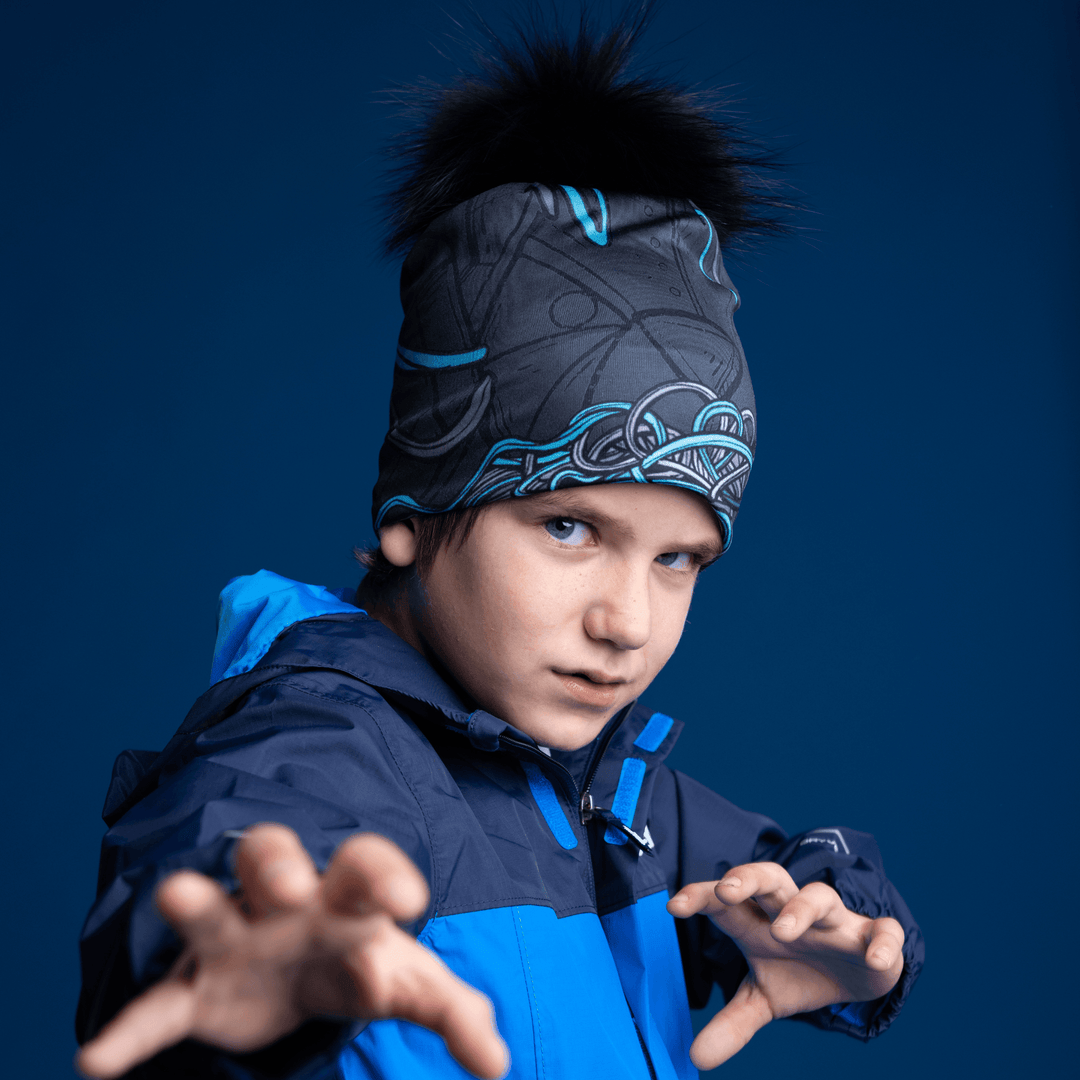 A young boy wearing the black and blue patterned Robocats Beanie and a blue jacket, with his hands reaching forward against a dark blue background.
